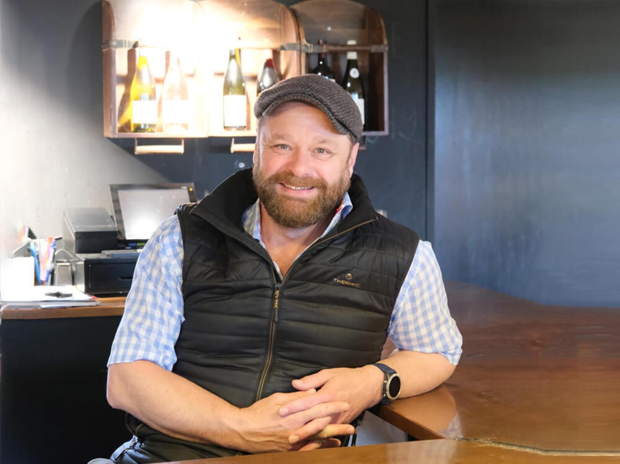 Rustic café interior design with leather sofas, wooden tables, and industrial lamps creating a warm and atmospheric setting among shelves stocked with wine and delicacies.